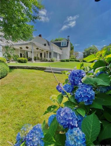 a large house with blue flowers in the yard at The Connecticut River Valley Inn Hartford South/Glastonbury in Glastonbury