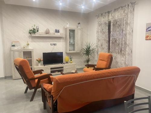 sala de estar con sillas de color naranja y TV de pantalla plana en La Pigna Casa Vacanza, en Nicolosi