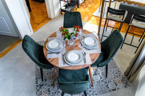 une table en bois avec des chaises vertes, des assiettes et des fleurs dans l'établissement DejaVu, à Novi Sad