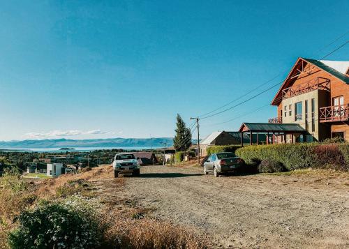 two cars parked on a dirt road next to a house at Lupama in El Calafate