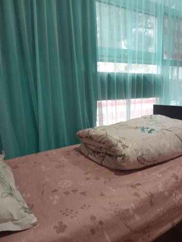 a bed with a pillow and a window with green curtains at New Saburtalo Star in Tbilisi City