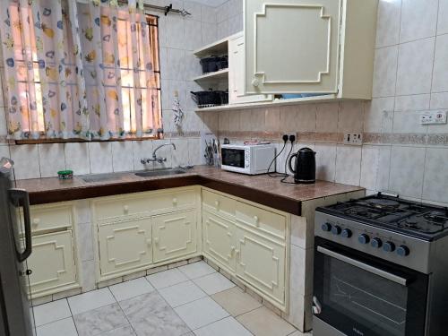 uma cozinha com armários brancos, um fogão e um micro-ondas em Tamiasuites Apartment em Kisumu