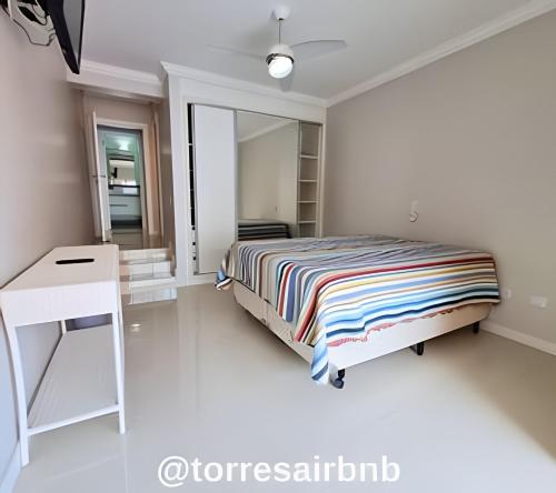 1 dormitorio con cama, escritorio y espejo en Cobertura a poucos metros do mar, en Torres