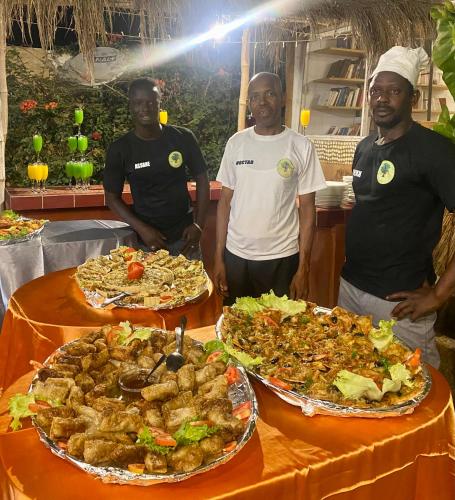 three men standing in front of three plates of food at LE BENTENIER Home Détente in Nianing