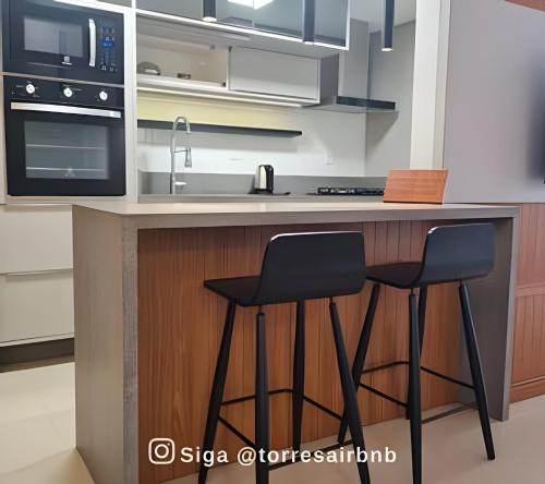 a kitchen with two black chairs at a counter at Apto 02 quartos | Ar | 500mts do mar | Aceita Pet in Torres