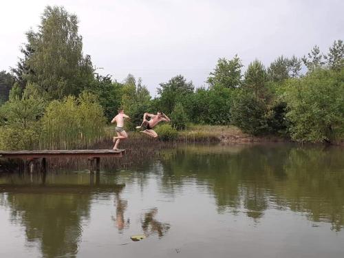two people jumping off a dock into a body of water at Agroturystyka Leśna Malinka in Celejów