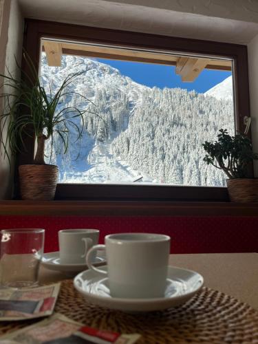 a table with a view of a snowy mountain through a window at Pension DORFPLATZL Pitztal in Plangeross