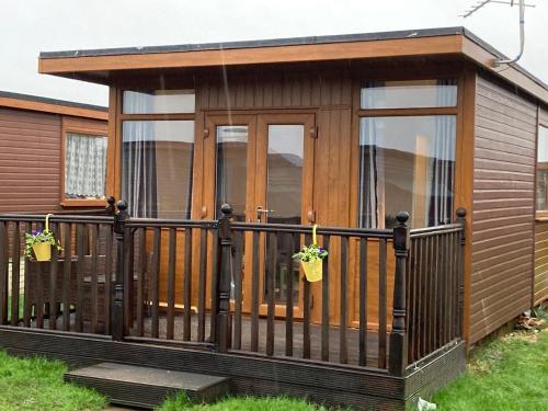 a small cabin with a wooden deck with windows at J16 Mablethorpe Pet Friendly Chalet in Mablethorpe