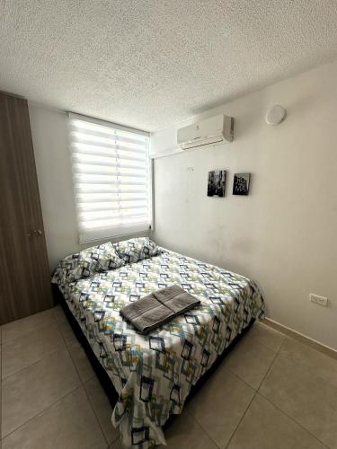 ein Schlafzimmer mit einem Bett mit einer Bettdecke und einem Fenster in der Unterkunft Hermoso Apartamento cerca del centro comercial jardin plaza in Cúcuta
