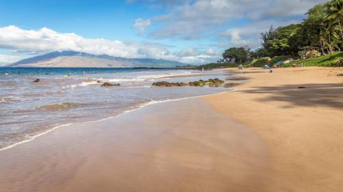 a sandy beach with people swimming in the ocean at NEW Luxury Condo at Kameole Beach in Wailea