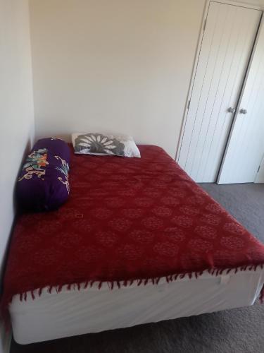 a bed with a red blanket and pillows on it at 10 Tapuwae in Auckland