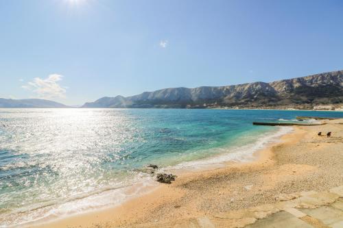 a beach with blue water and mountains in the background at Apartments by the sea Baska, Krk - 22409 in Baška