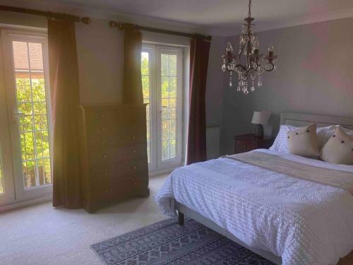 um quarto com uma cama branca, janelas e um lustre em Stunning Racecourse Townhouse for Royal Ascot em Winkfield