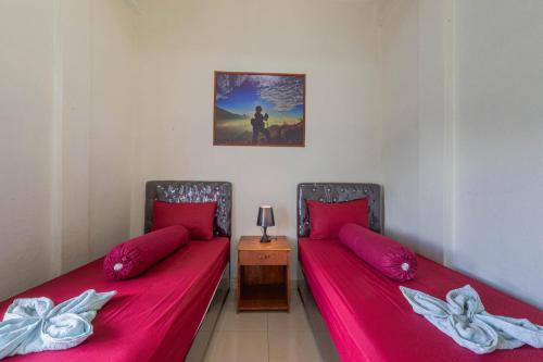two beds in a room with red sheets at Teras Sawah Guest House Syariah in Sembalun Lawang