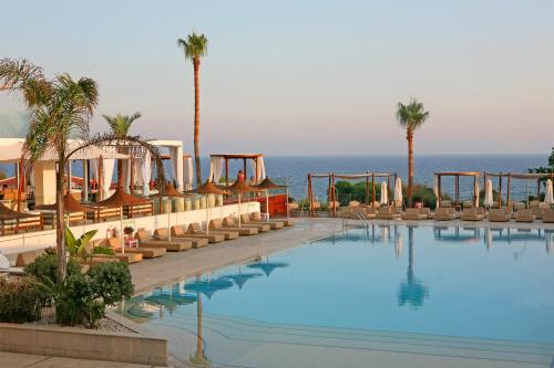 a hotel with a swimming pool with palm trees and the ocean at Napa Mermaid Hotel & Suites in Ayia Napa