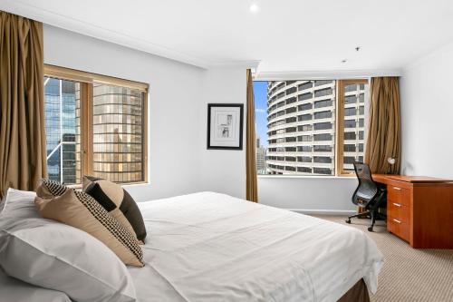 a bedroom with a bed and a desk and two windows at Quay West 2302 Self-Catering in Sydney