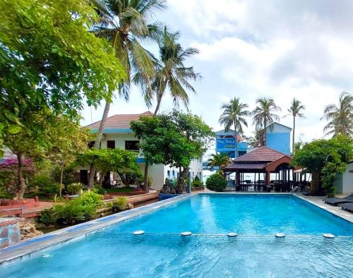einem Pool vor einem Gebäude mit Palmen in der Unterkunft Sóng Biển Xanh Mũi Né Resort - by Bay Luxury in Ấp Long Sơn