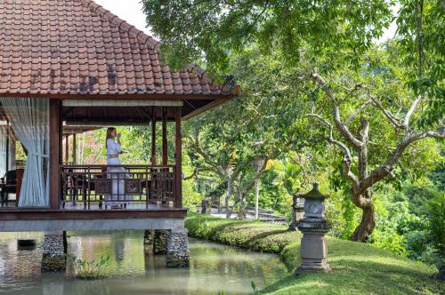 Eine Frau, die auf einem Pavillon neben einem Fluss steht. in der Unterkunft Santi Mandala Villa & Spa in Sukawati