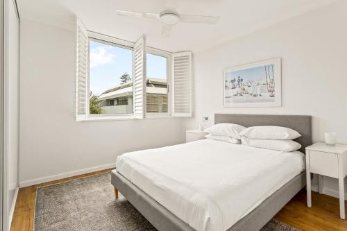 a white bedroom with a bed and two windows at Chic apartment footsteps from Manly Beach in Sydney