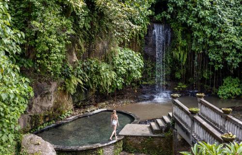 una mujer parada en una piscina frente a una cascada en Santi Mandala Villa & Spa, en Sukawati