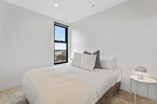 a white bedroom with a large bed and a window at Elegant Collingwood Apartment with City Views in Melbourne