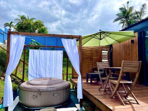 eine Terrasse mit einem Tisch, einem Sonnenschirm und einer Badewanne in der Unterkunft Lodge Agapë in Le Tampon