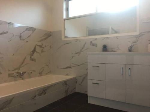 een badkamer met een bad, een wastafel en een spiegel bij Geelong Delight: Embrace Comfort @ Braund Avenue in Norlane