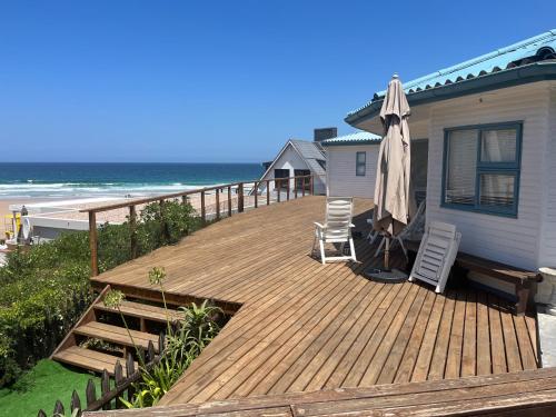 a wooden deck with chairs and an umbrella on the beach at MakiSaki Beach House in Herolds Bay