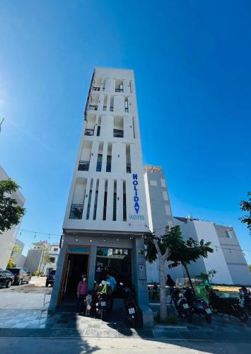 a tall white building with people standing outside of it at HOLIDAY HOTEL PHAN THiẾT in Ấp Bình Hưng