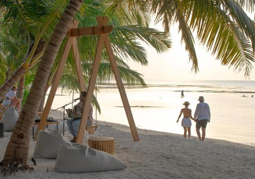 a group of people walking on a beach with palm trees at Stone Hotels Dhiffushi in Dhiffushi