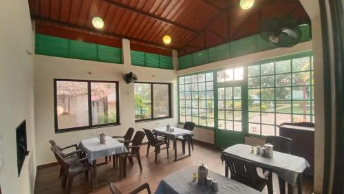 ein Esszimmer mit Tischen, Stühlen und Fenstern in der Unterkunft Singanama RESORT in Pachmarhi