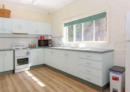 a kitchen with white cabinets and a sink and a window at Quiet Country Retreat in Forster