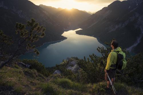 a man with a backpack standing on a hill overlooking a lake at Pension Kreuzeck - Dein Glücksplatz am Lech in Weissenbach am Lech