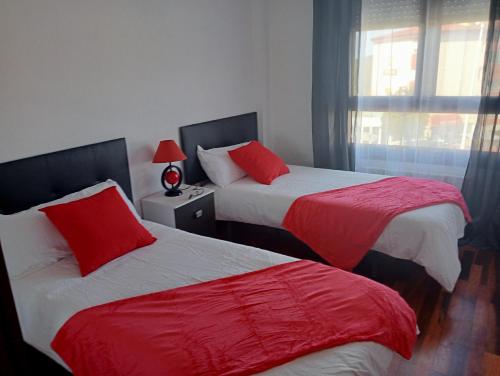 two beds with red pillows in a room at Piso Loredo in Loredo