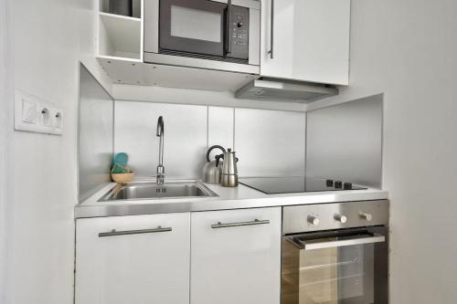 uma cozinha branca com um lavatório e um micro-ondas em Cosy studio avec parking au sous-sol em Paris