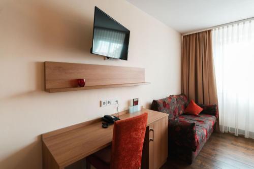 Zimmer mit einem Schreibtisch, einem TV und einem Sofa in der Unterkunft Landhotel und Weingasthof Schwarzer Adler in Wiesenbronn