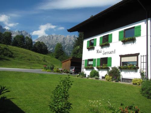 a white building with green shuttered windows and a yard at Haus Sonnwend in Ellmau