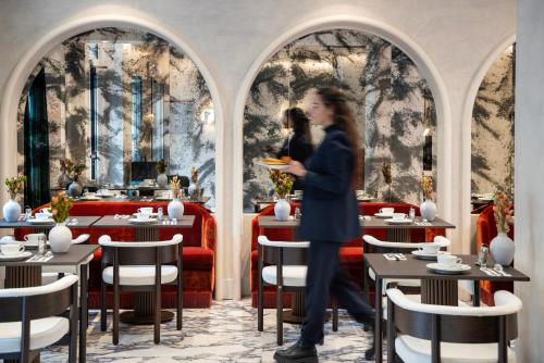 a woman walking through a restaurant with tables and chairs at Hotel des Carmes by Malone in Paris