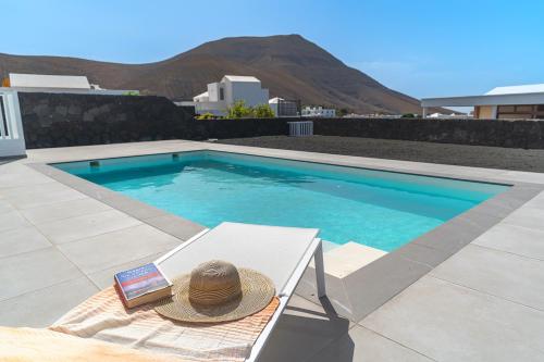 a hat and a book sitting on a bench next to a swimming pool at Vv Villa Secretos de Yaiza 1 by Hh - private pool & BBQ in Yaiza