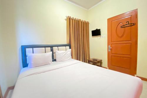 1 dormitorio con 1 cama blanca grande y puerta de madera en RedDoorz Syariah at D'Rizs Homestay en Bukittinggi