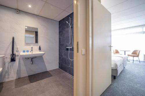 een badkamer met een wastafel, een douche en een bed bij Fletcher Hotel - Restaurant de Zeegser Duinen in Zeegse