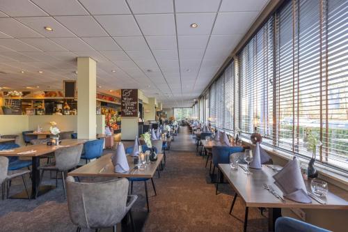 a dining room with tables and chairs and windows at Fletcher Hotel - Restaurant de Zeegser Duinen in Zeegse