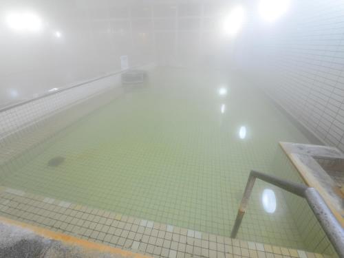 a swimming pool with green tiles in a foggy room at HigashimaeOnsen Shinwanoyu Hotel Akitaya in Hokuto