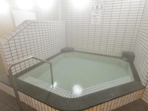 a bath tub in a white tiled room with at HigashimaeOnsen Shinwanoyu Hotel Akitaya in Hokuto