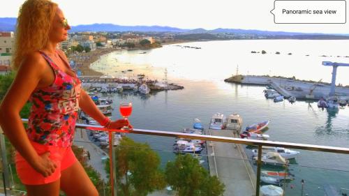 una donna in piedi su un balcone con un bicchiere di vino di Panoramic Sea View a Chania