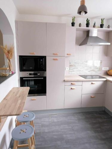 une cuisine avec des placards blancs, une table et des tabourets dans l'établissement Maison à coté de Disneyland Paris, Stade de France, Jeux Olympiques, à Claye-Souilly