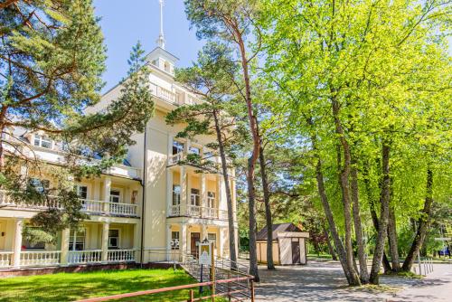 un grand bâtiment blanc avec des arbres devant lui dans l'établissement Žuvėdra, à Palanga