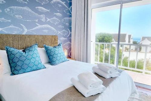 - une chambre dotée d'un lit blanc avec des oreillers bleus et d'une fenêtre dans l'établissement House Khasia- on the Golden Mile, à St Helena Bay