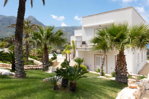 a white house with palm trees in a yard at La Blanca Resort & Spa in Castellammare del Golfo