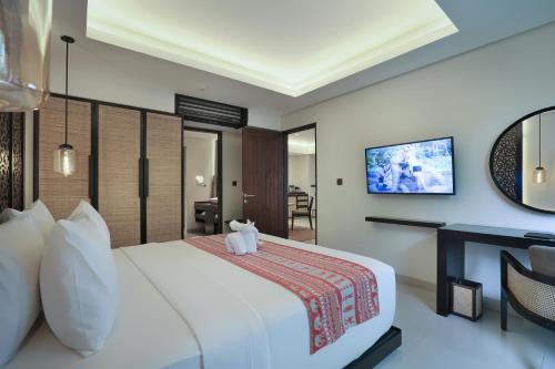 a hotel room with a white bed and a television at Sanctoo Suites & Villas in Gianyar